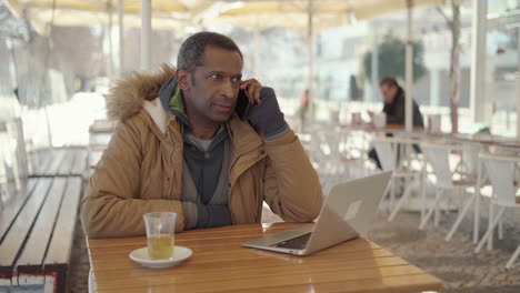 Hombre-Afroamericano-Sonriente-Hablando-Por-Teléfono-Inteligente-En-La-Cafetería